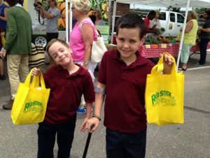 Two kids smiling with their bags from the Red Stick Mobile Farmers Market.