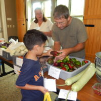 Man handing kid a red bell pepper.