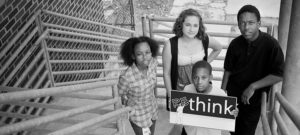 Group of young people posing with sign in black and white.